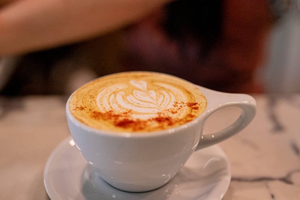 Close-up of a latte with intricate foam art in a white cup at a stylish café.