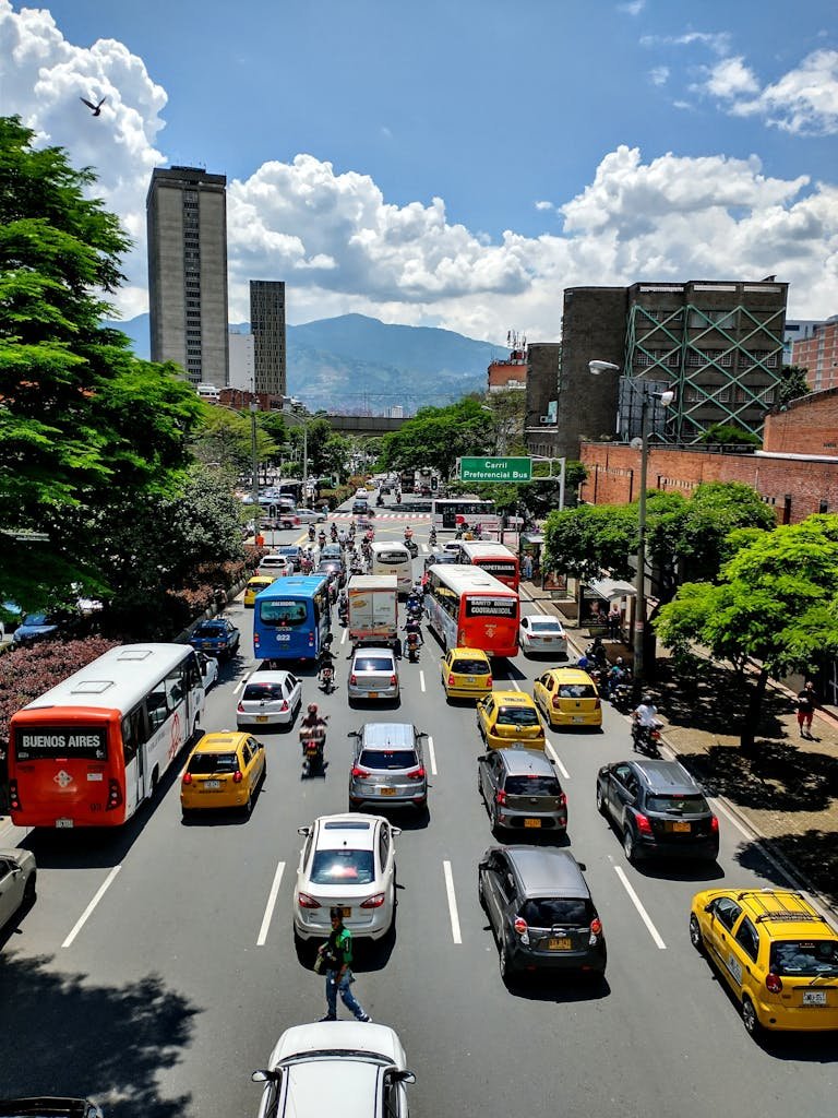 Street scene in Medellín, Colombia, showcasing bustling traffic, taxis, and towering buildings on a sunny day.