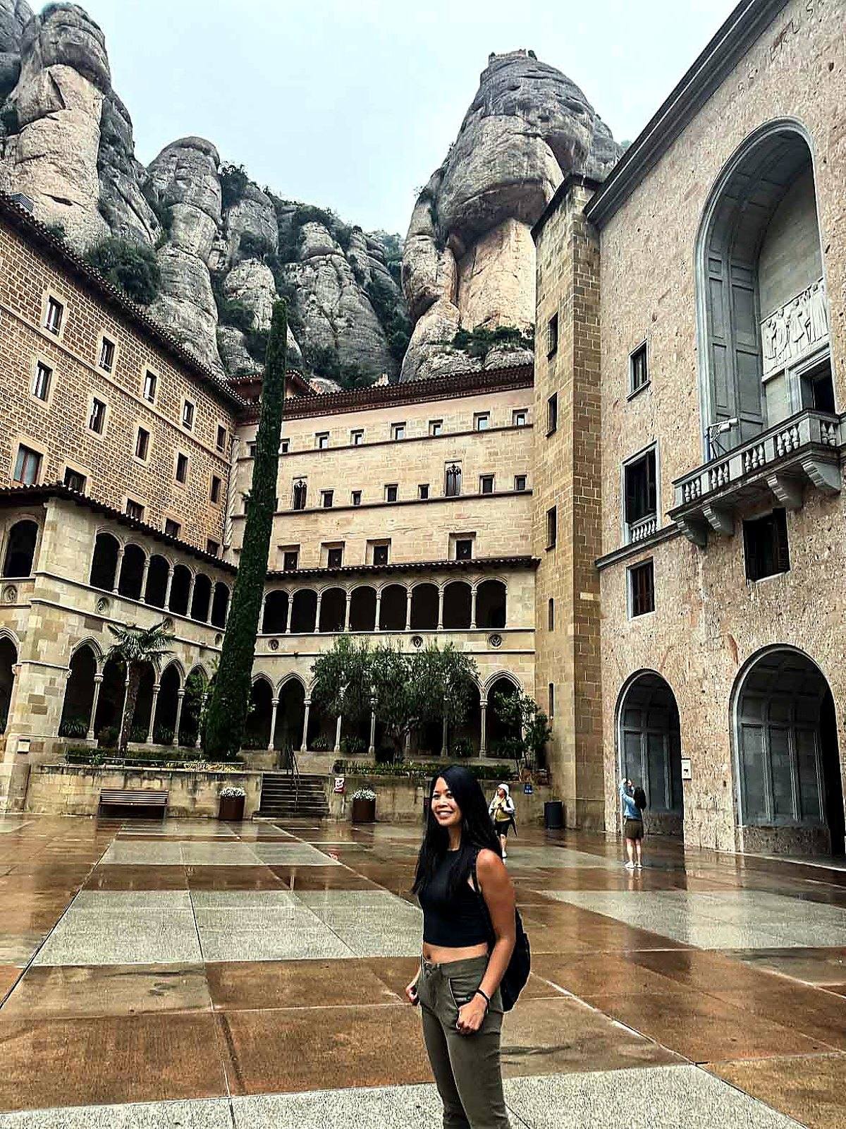 Marie in the Montserrat monastery courtyard with rock formations rising behind the buildings.