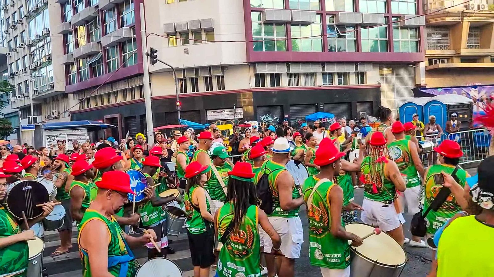 Carnival percussionists in red and green costumes parading through a Rio street