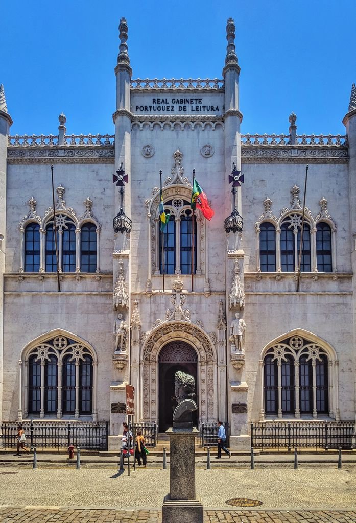 Exterior design of entrance of old stone building of Royal Portuguese Cabinet of Reading with arched windows and sculptures and national flags located in Rio de Janeiro in Brazil